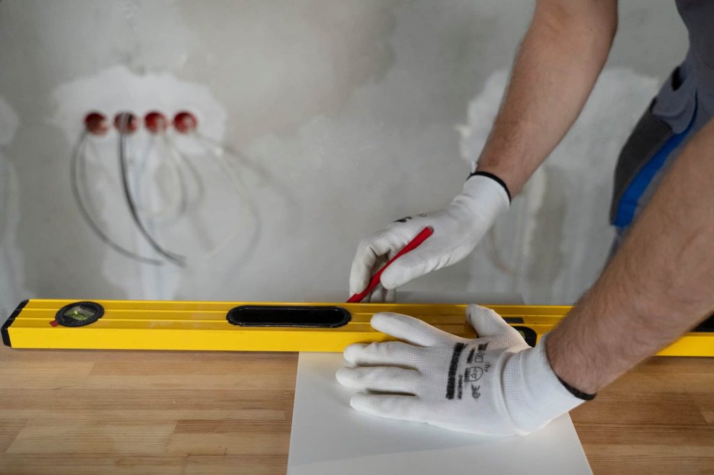 Worker marking tile placement with a level and pencil, ensuring accurate As-Built measurements for precise wall tile layout.