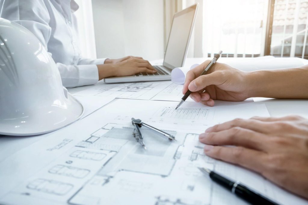 Engineers reviewing As-Built blueprints with drafting tools and a hard hat, focusing on restoration planning.