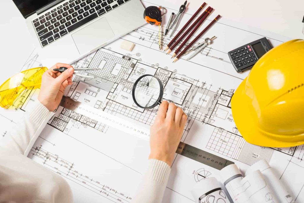 Architect reviewing building blueprints with tools, a hard hat, and a laptop, highlighting construction planning and design.