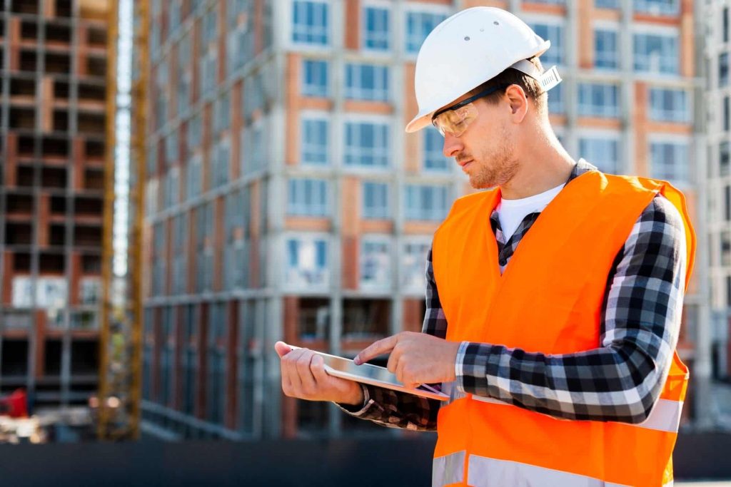 Construction inspector using a tablet to review building plans on-site, emphasizing modern inspection methods and technology integration.