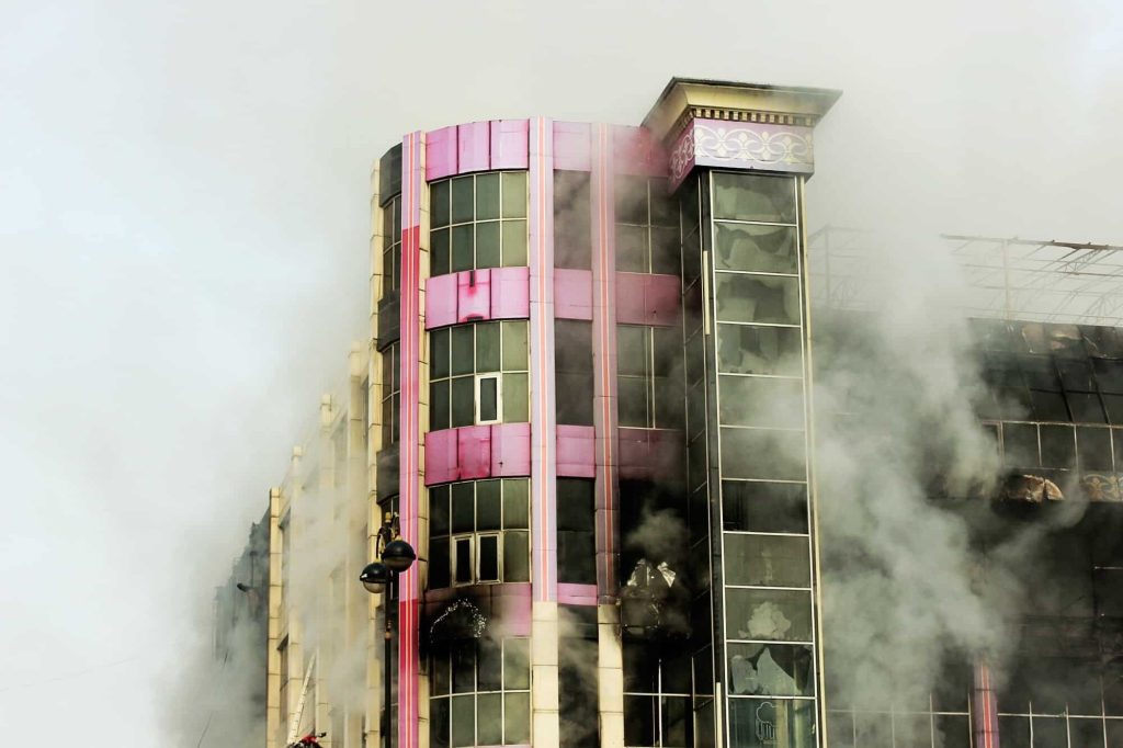 Severely fire-damaged high-rise building with visible smoke, ideal for fire damage assessment and restoration planning using laser 3D scanning.